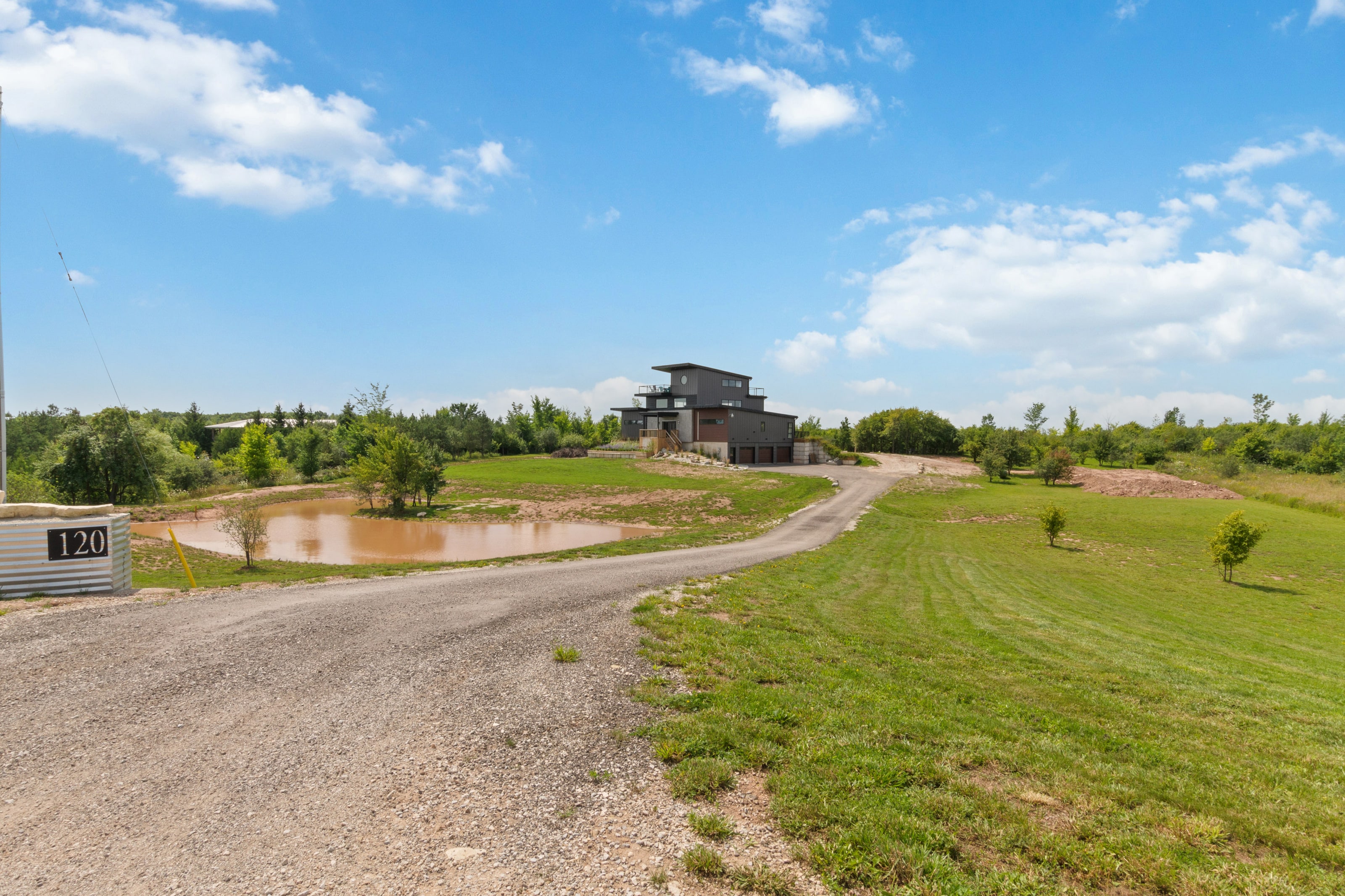 A gravel drive curving past a pond and open mown fields toward the house on a rise