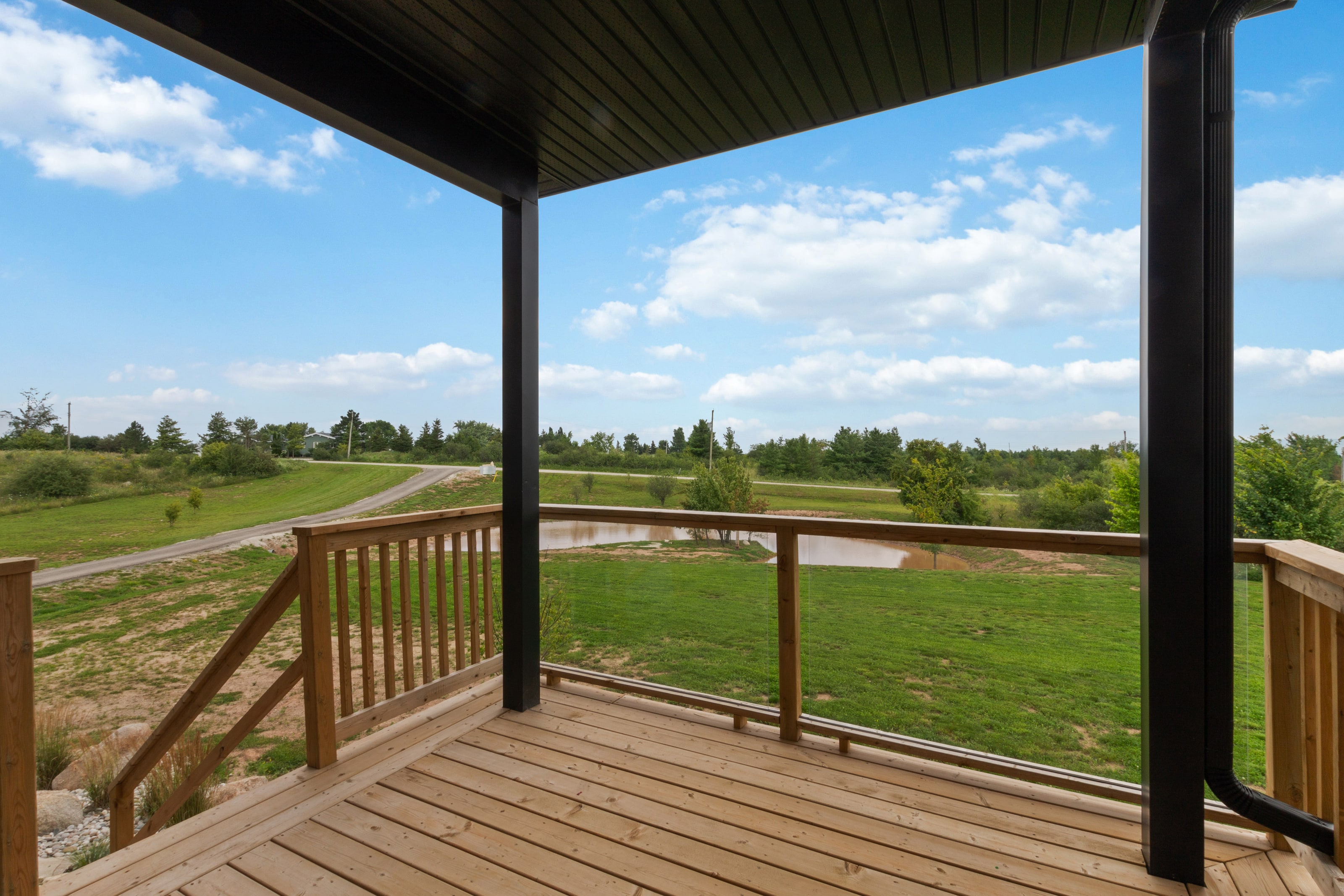 A covered cedar deck with timber posts looking out over the pond and drive