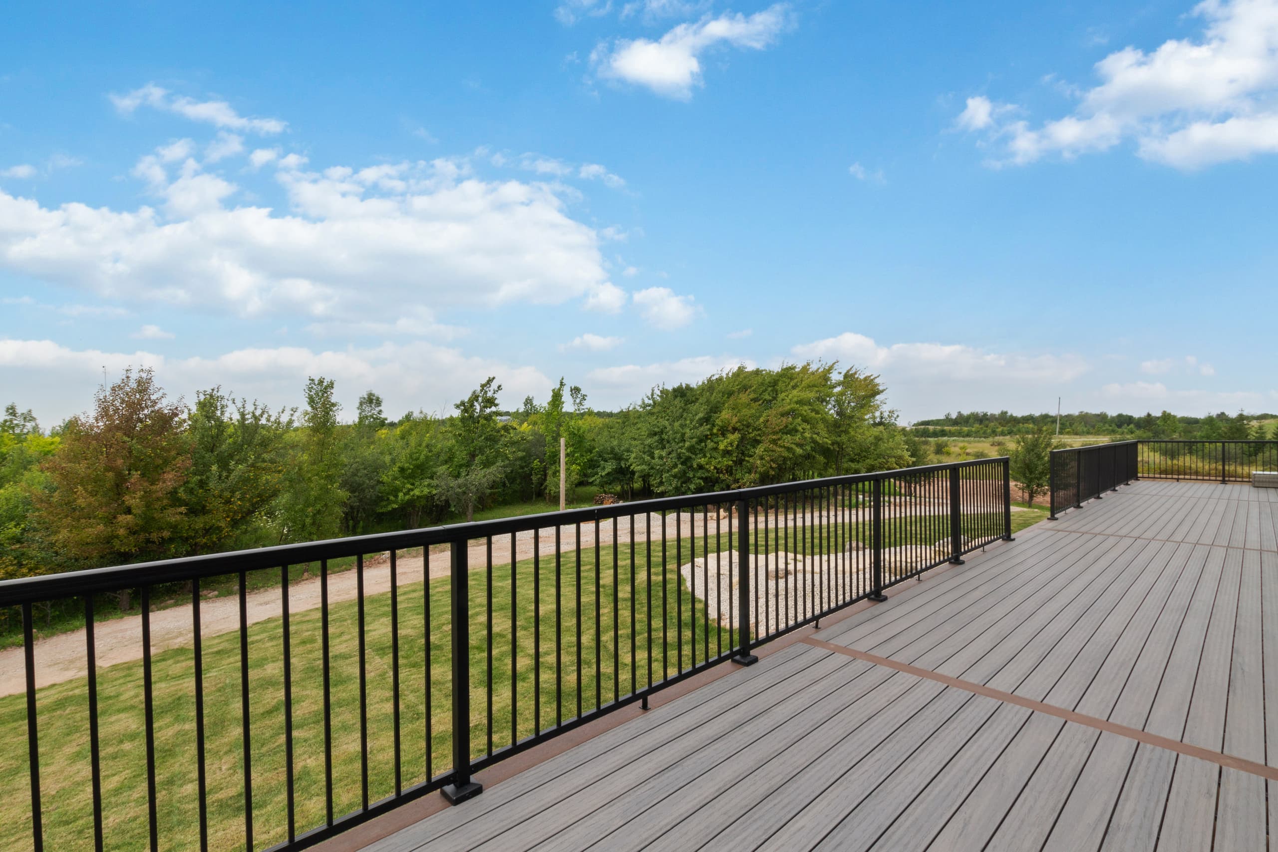 The composite deck running the length of the house with a black metal railing and fields beyond