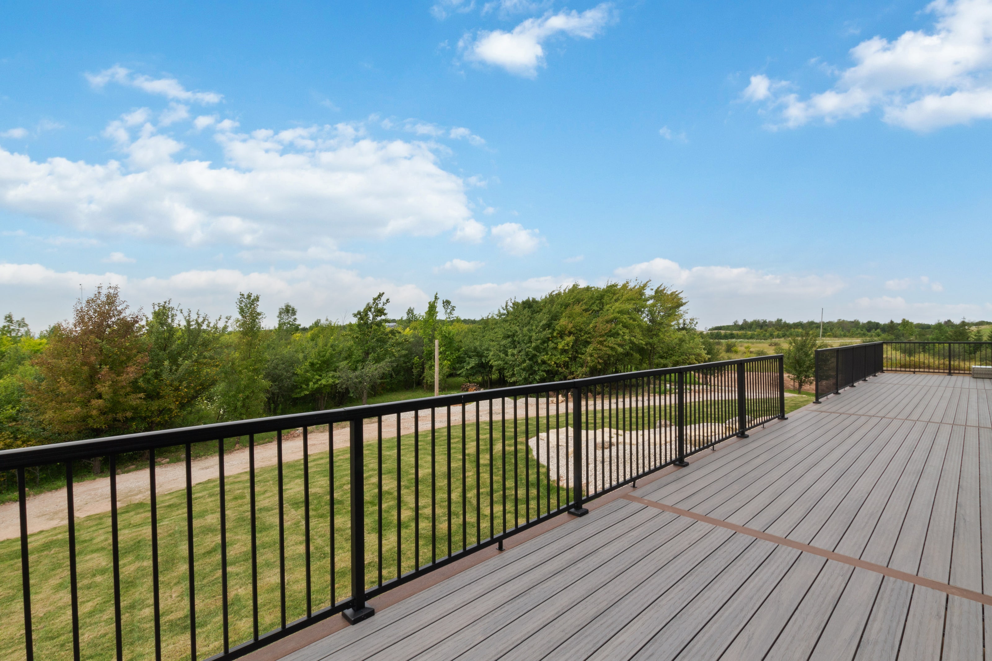 The composite deck running the length of the house with a black metal railing and fields beyond