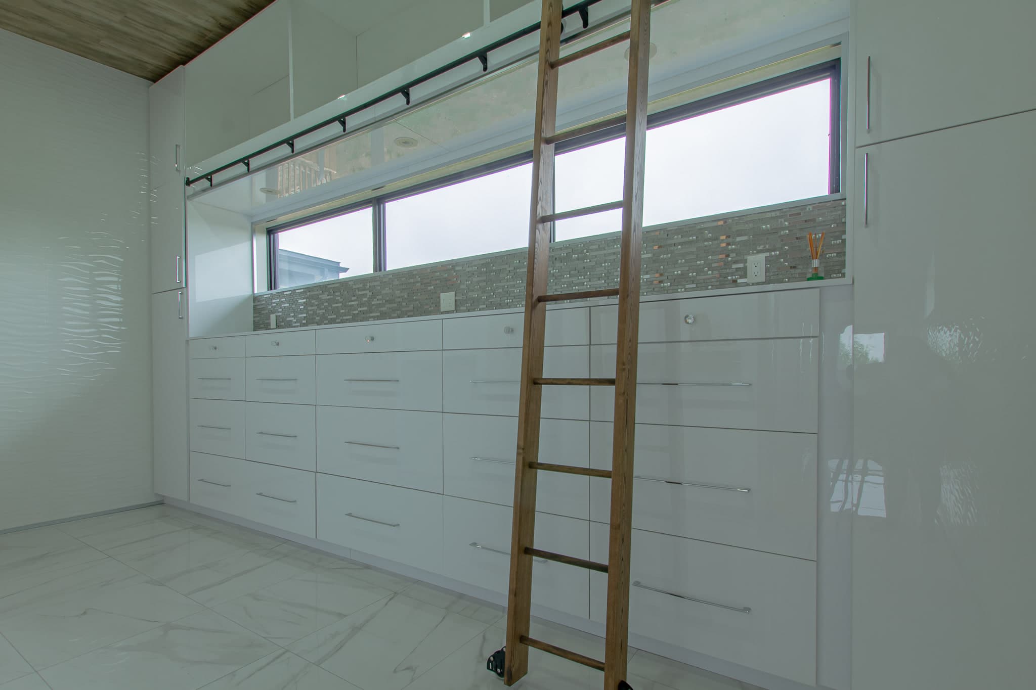 A dressing room walled in white cabinetry with a rolling timber library ladder and a ribbon window above