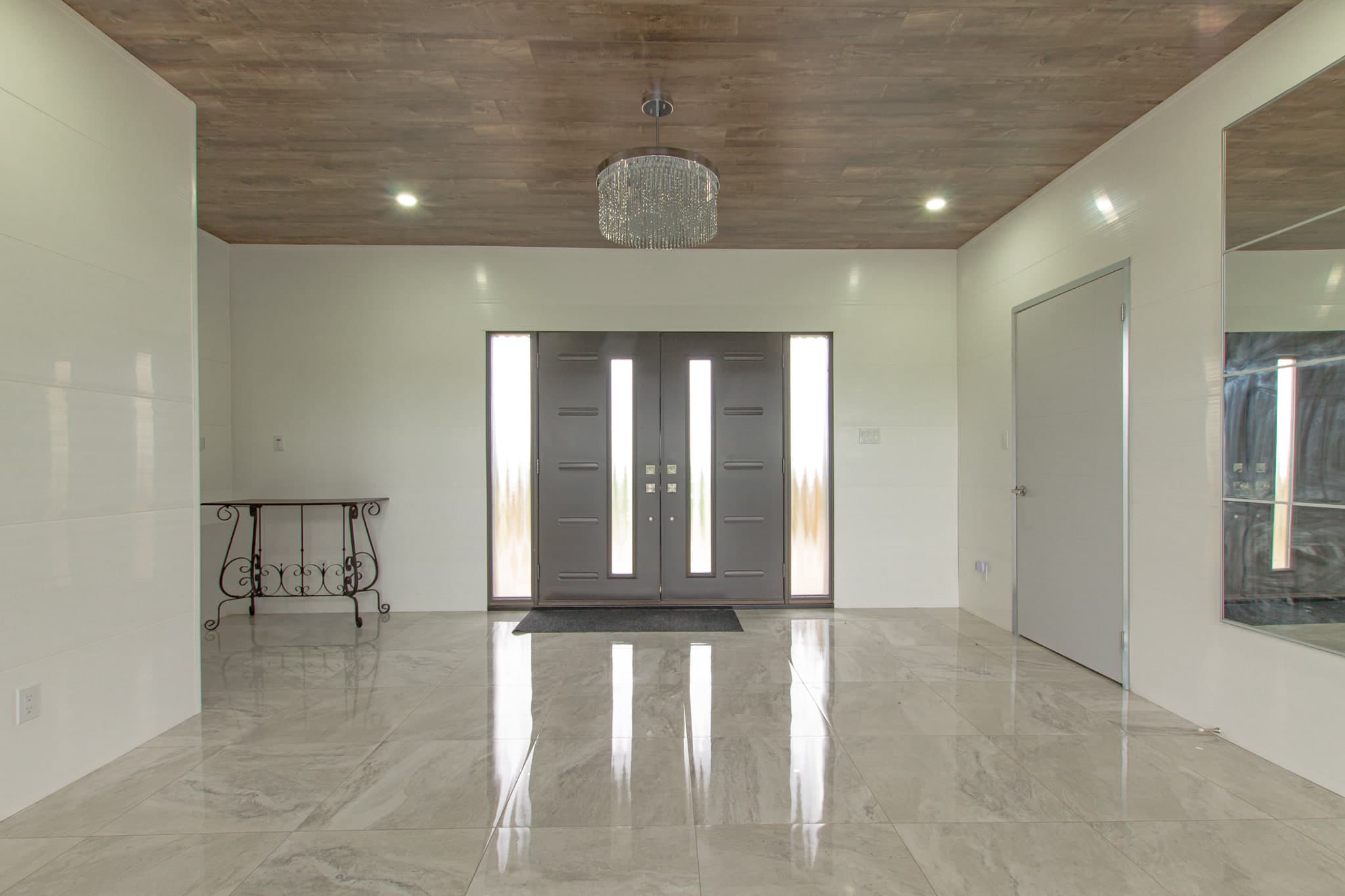 A wide tiled entrance hall facing a pair of glazed front doors, with a console table to one side