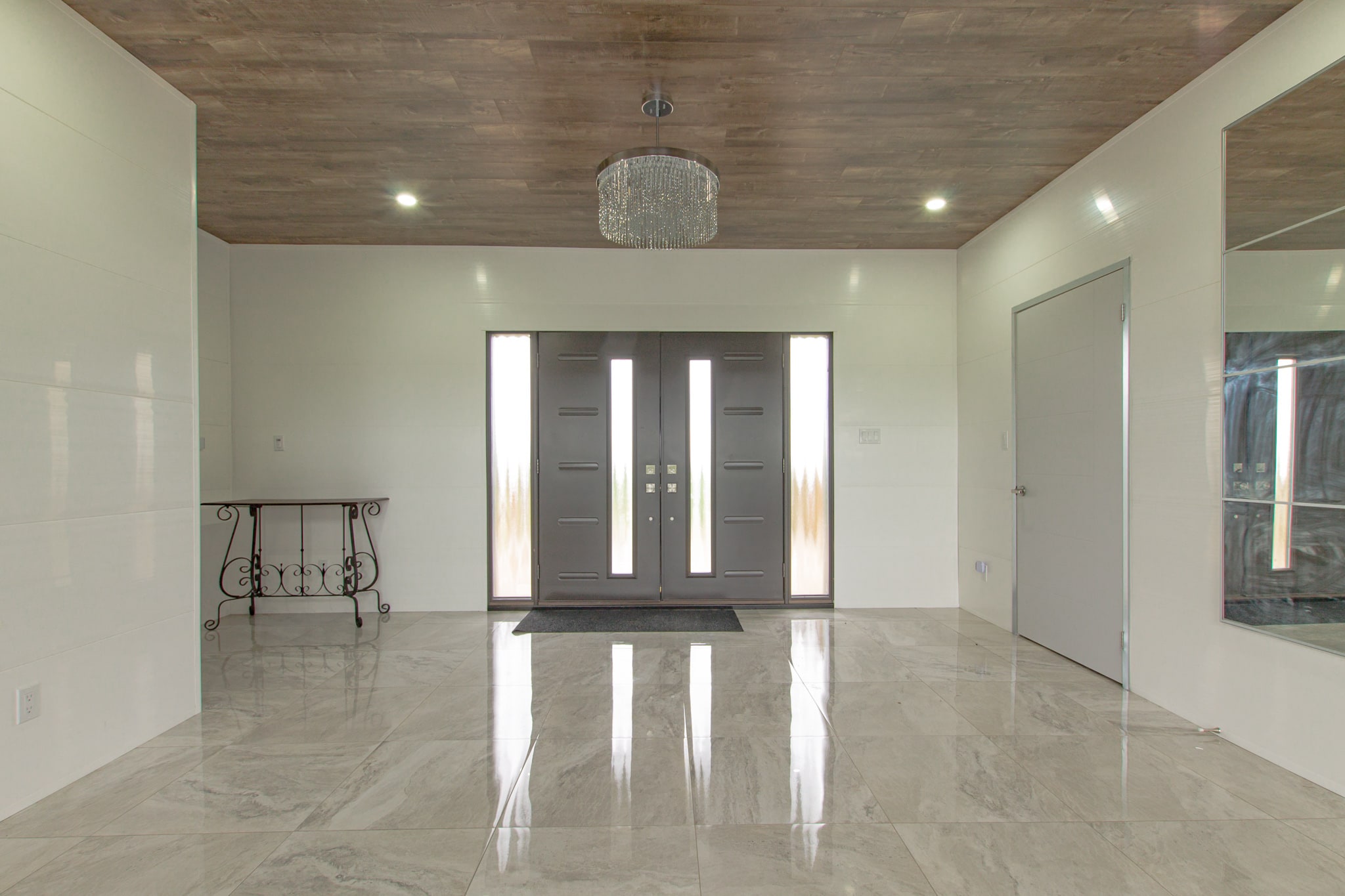 A wide tiled entrance hall facing a pair of glazed front doors, with a console table to one side