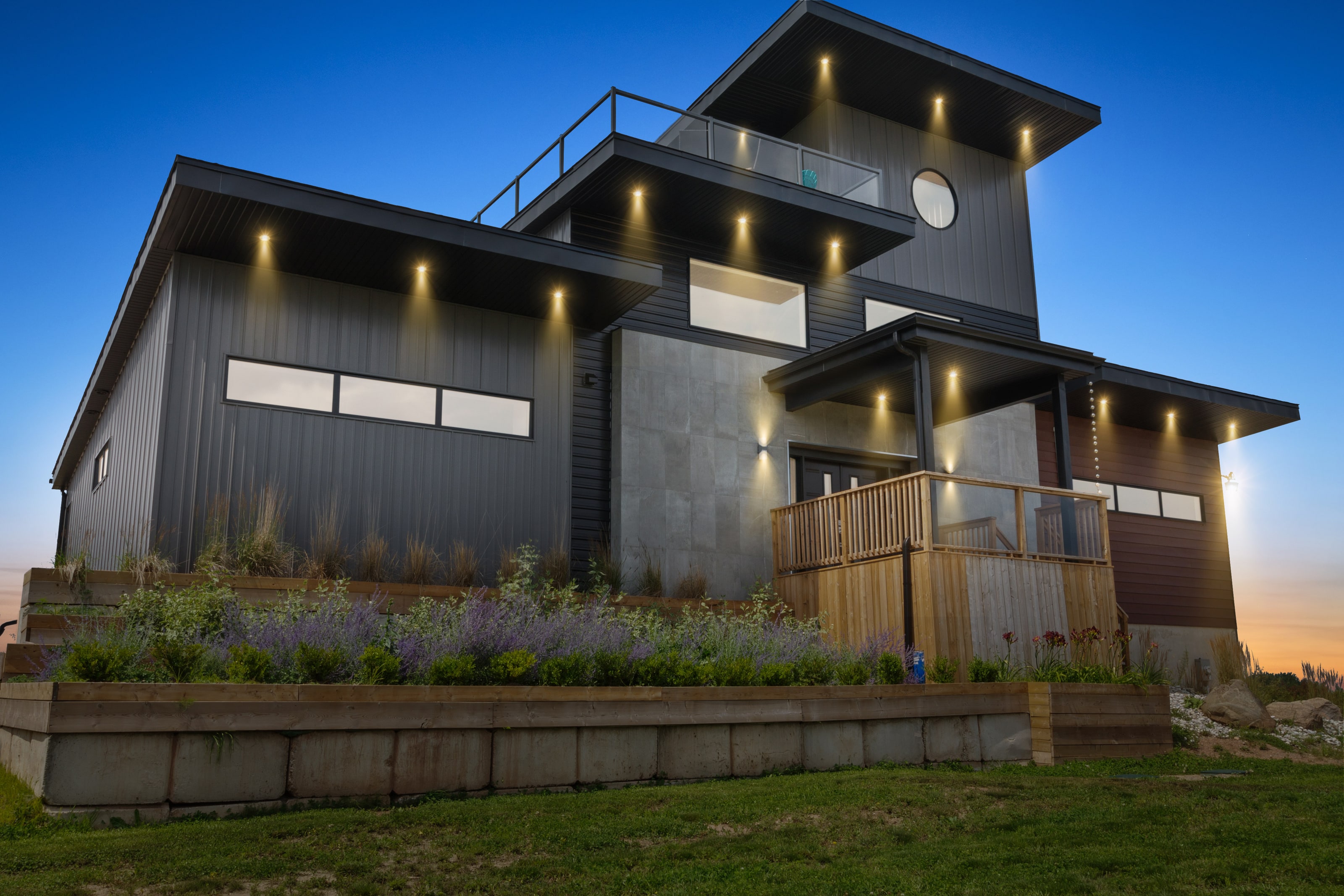 The house at dusk from an angle, showing the cantilevered roof planes, cedar deck and planted terrace wall