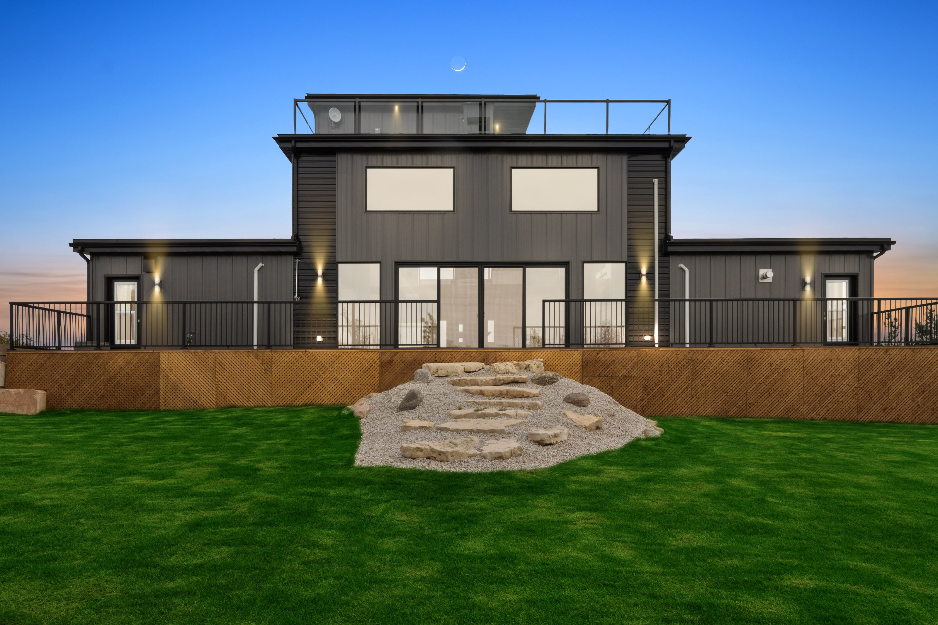 The rear of the house above a level lawn, with a run of glass doors and a stone stair set into the grass
