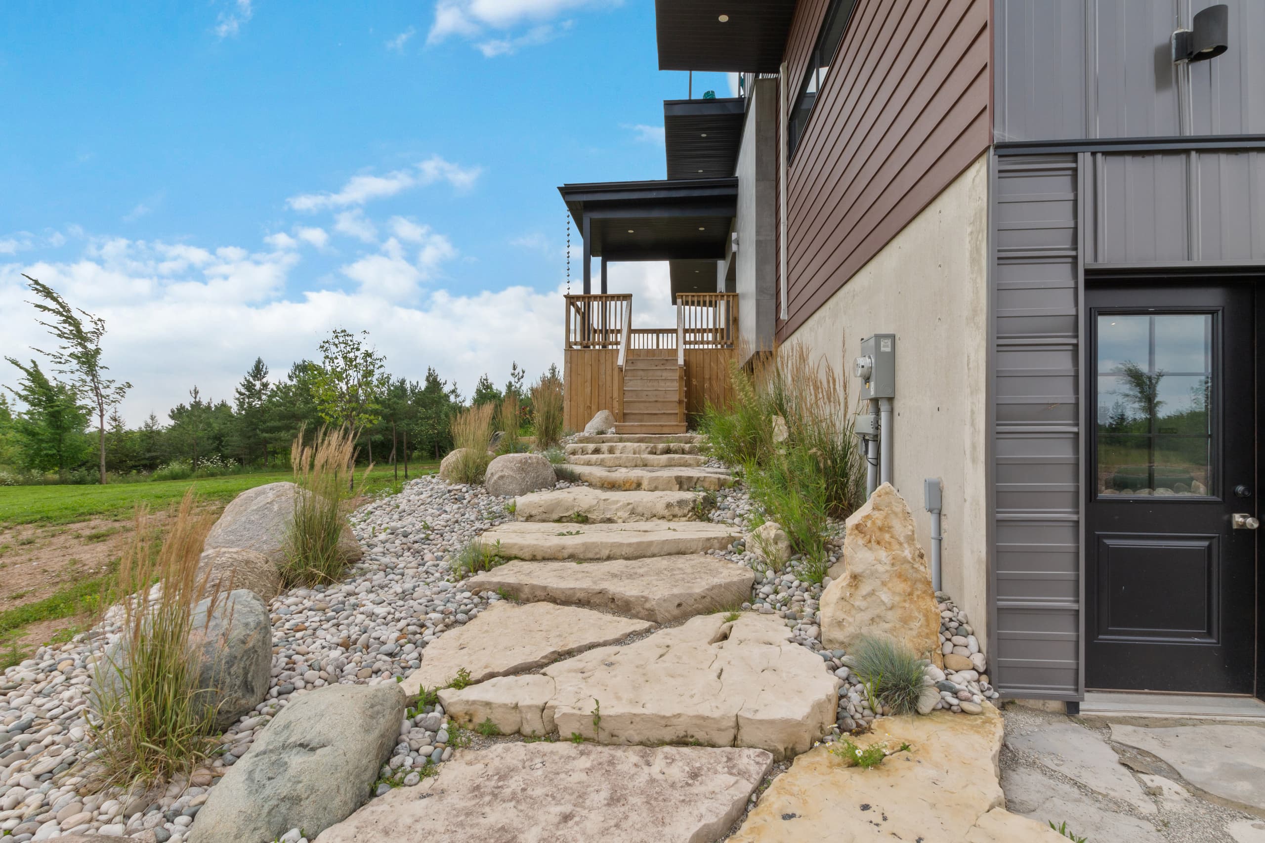 Flagstone steps and ornamental grasses climbing between boulders to a side entrance