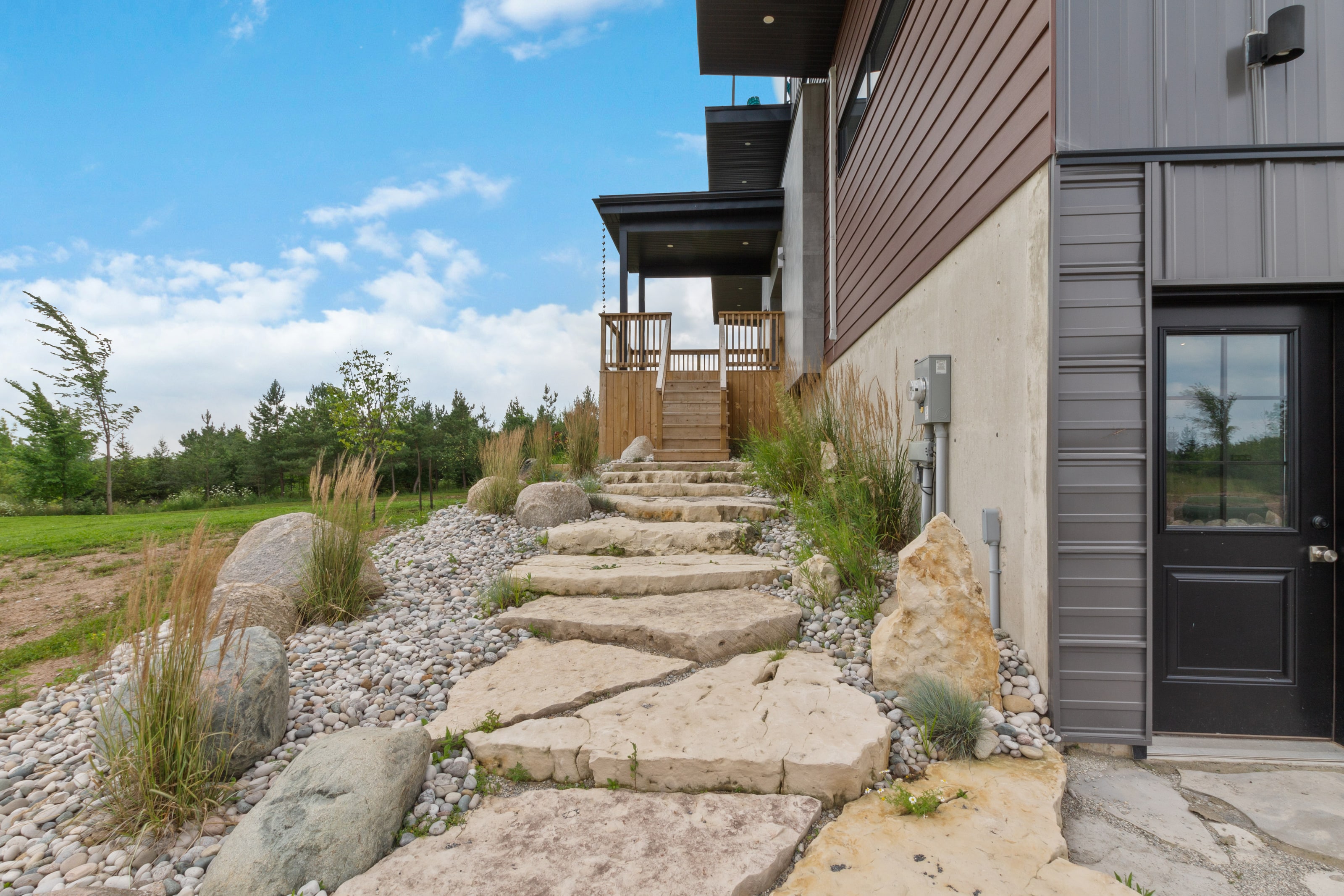 Flagstone steps and ornamental grasses climbing between boulders to a side entrance