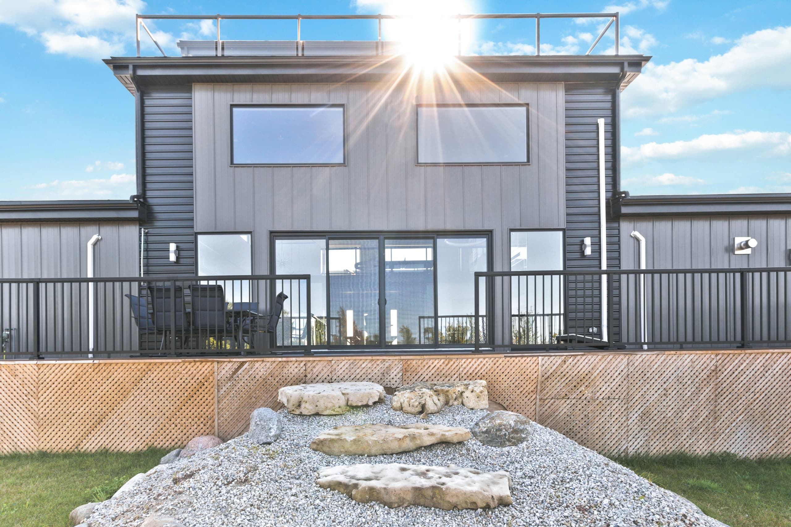 Sun breaking over the roofline above the deck, with a stone fire ring set in gravel below