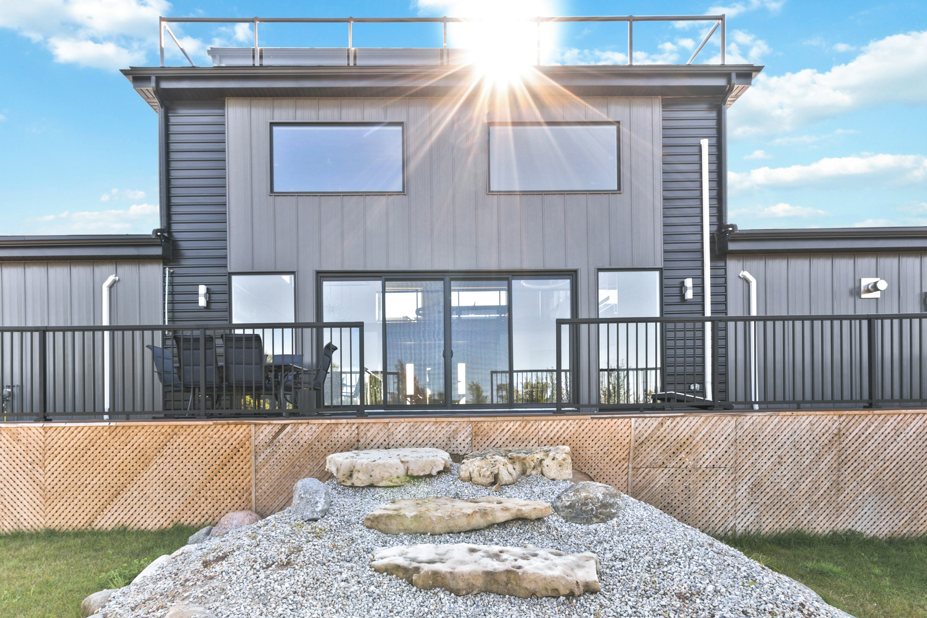 Sun breaking over the roofline above the deck, with a stone fire ring set in gravel below