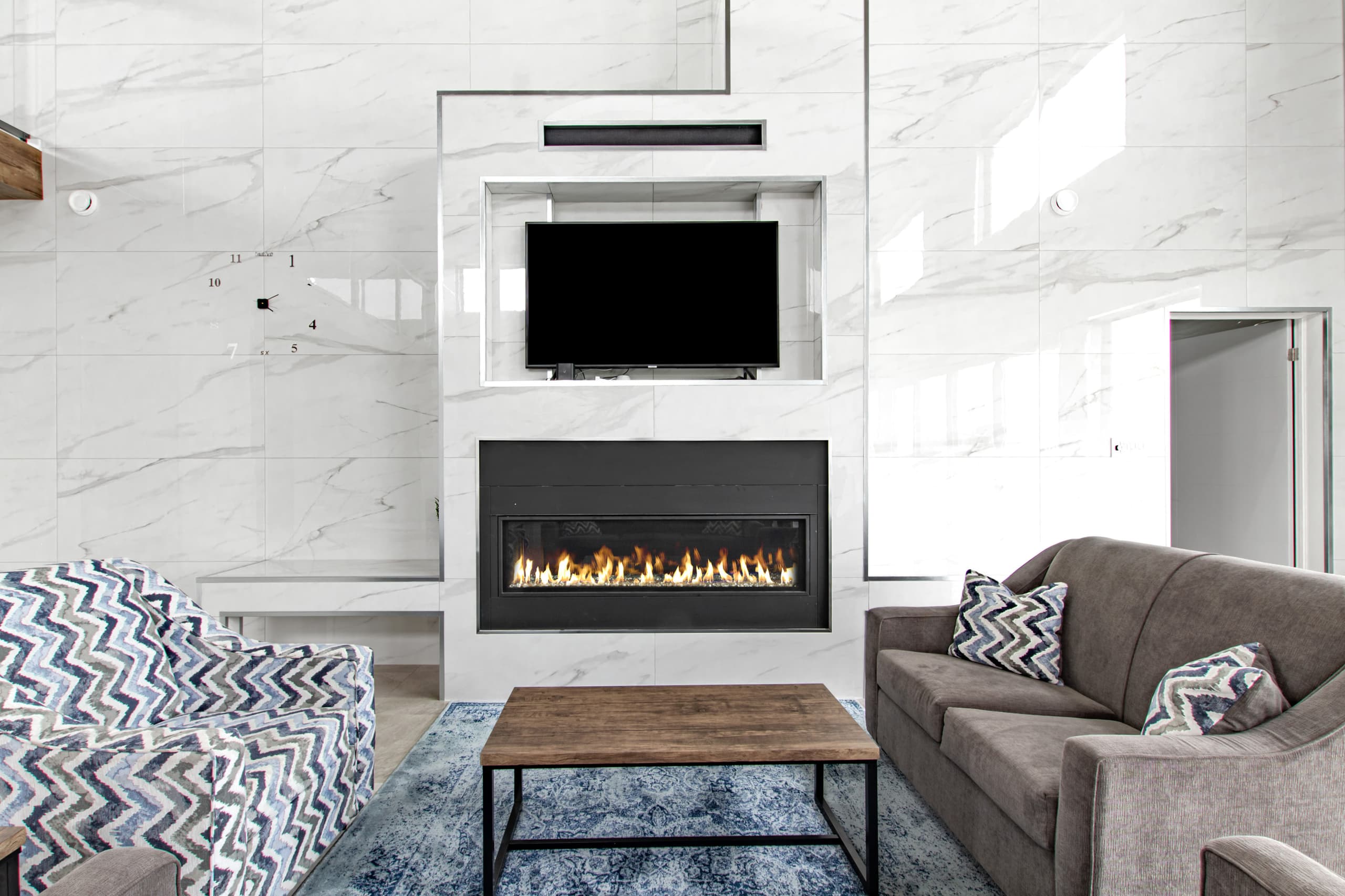 A lit linear gas fireplace set into a marbled stone surround, with a sofa and low table in front