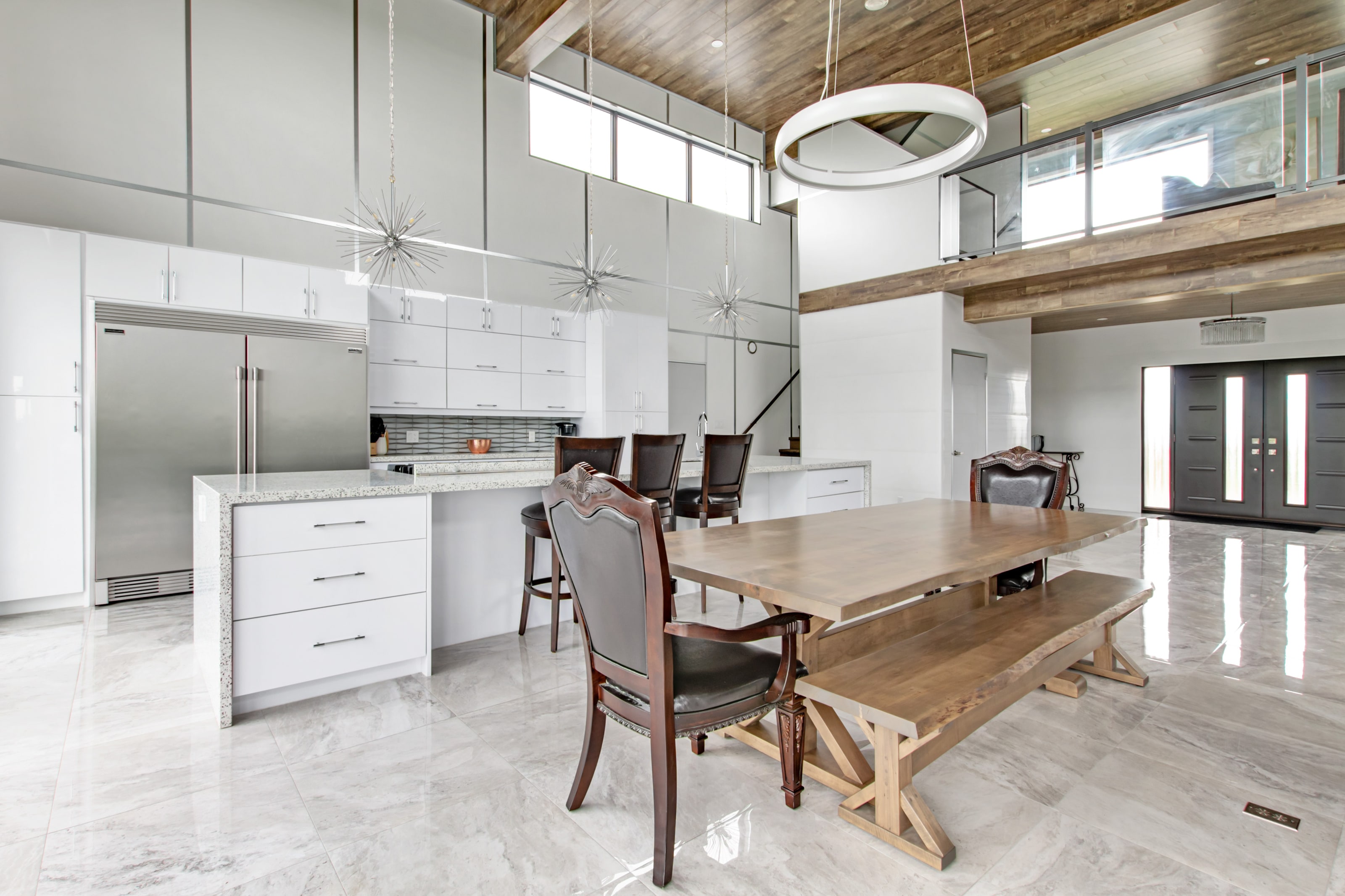 A long timber dining table with bench and chairs set between the kitchen island and the stair