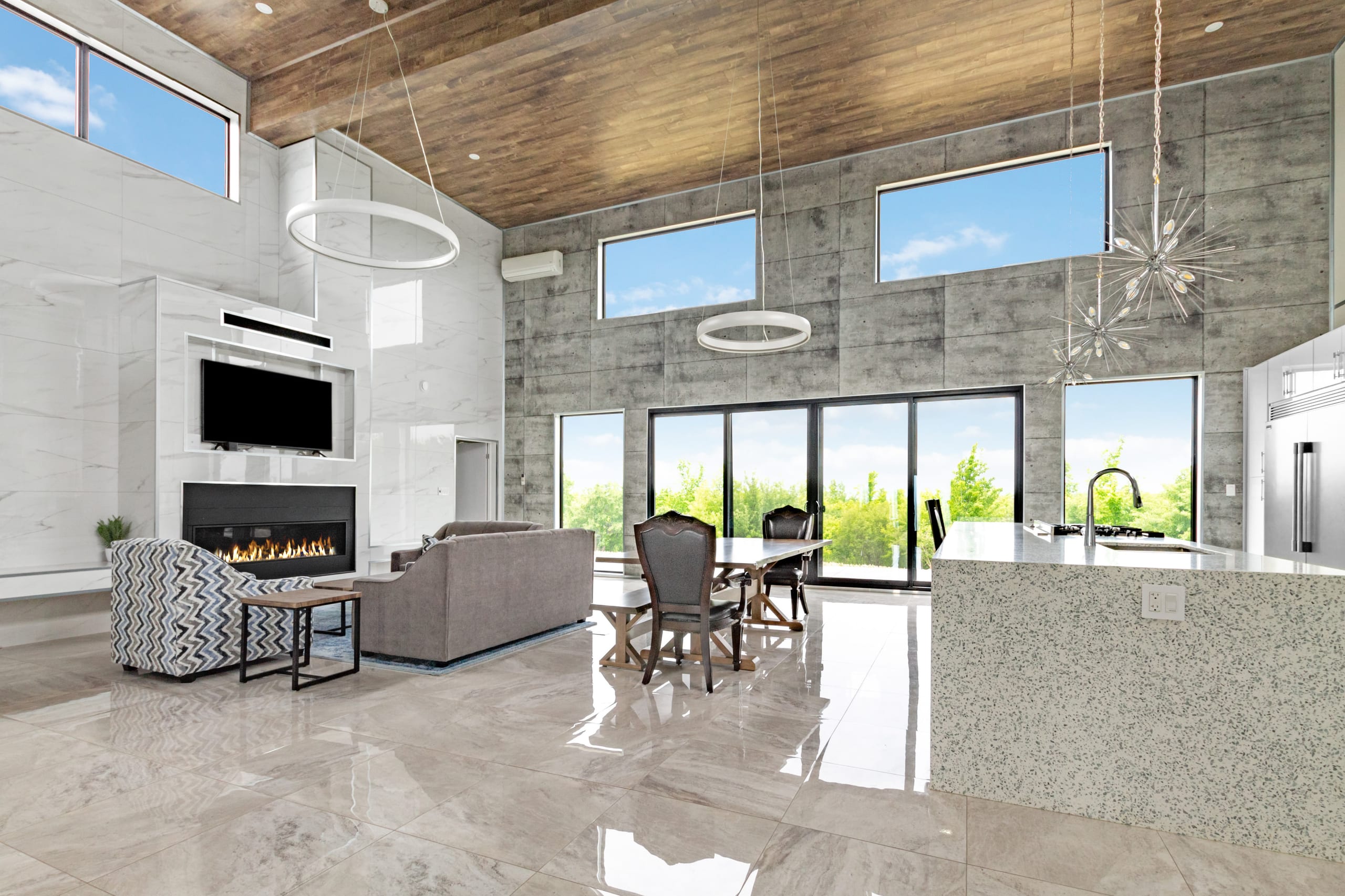 Lounge seating facing a linear gas fireplace and wall-mounted television, with the dining table and kitchen beyond