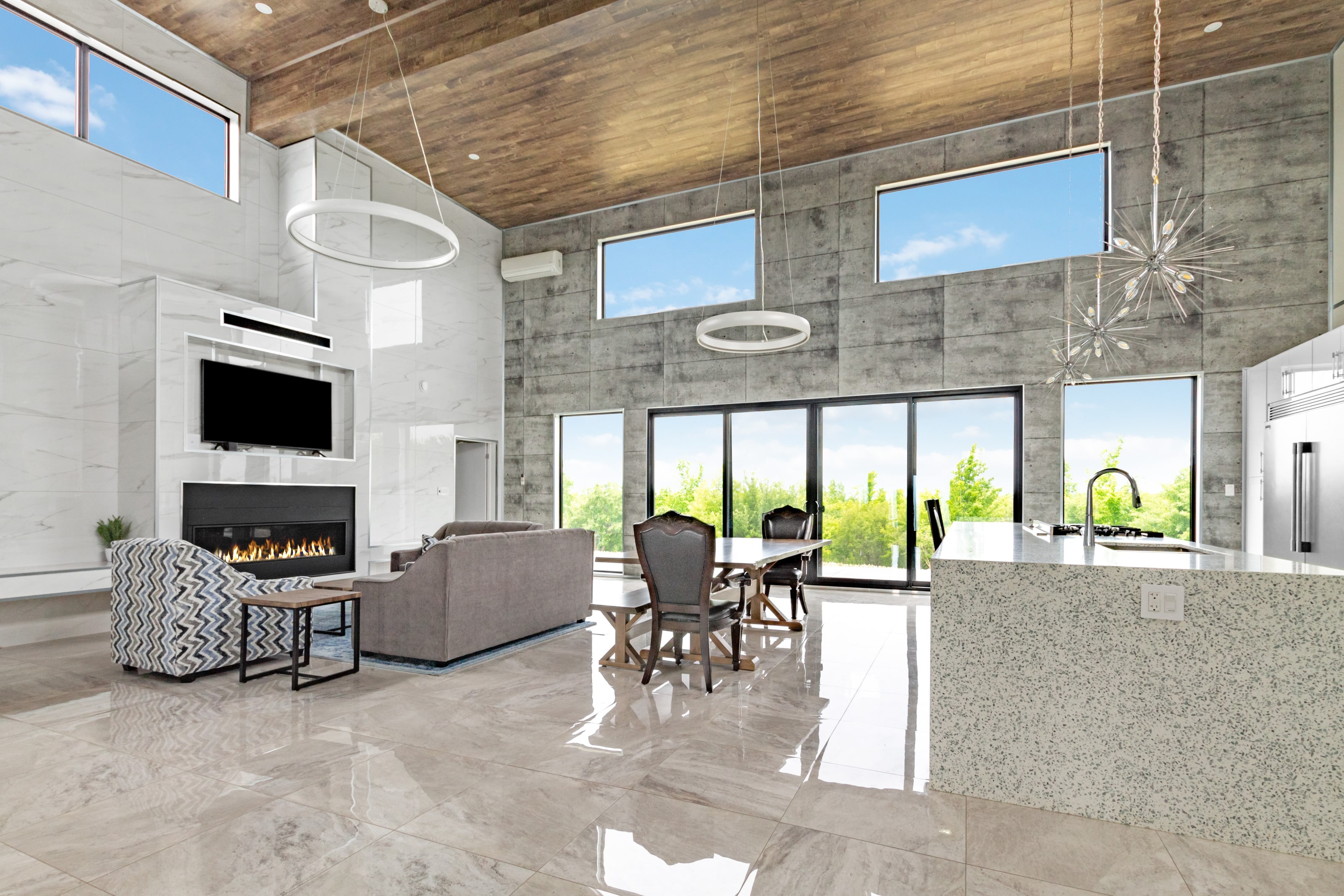 Lounge seating facing a linear gas fireplace and wall-mounted television, with the dining table and kitchen beyond