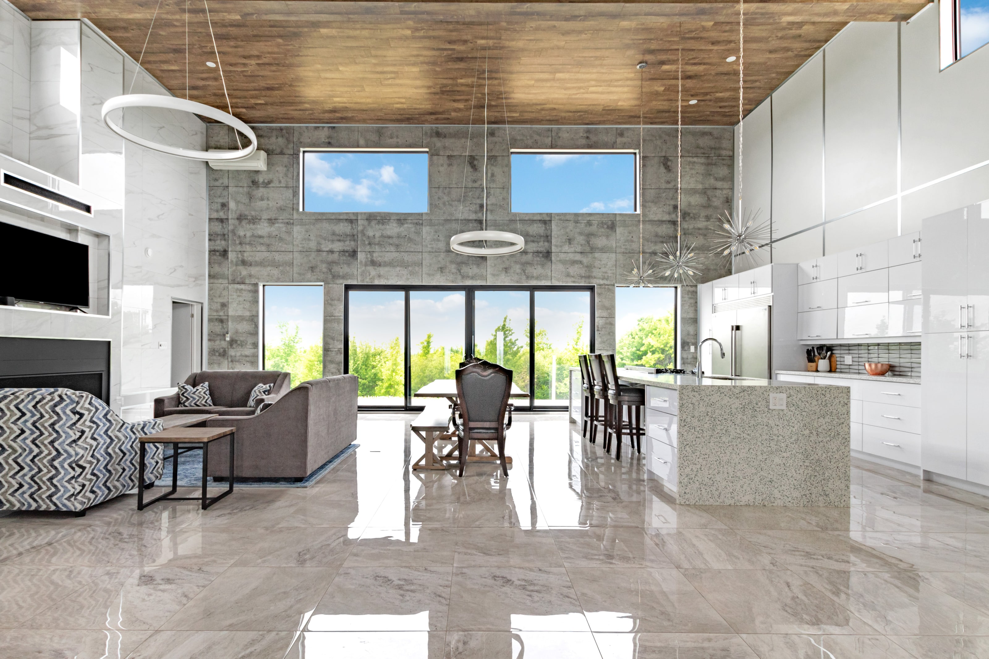 The double-height great room with a board-formed concrete wall, plank timber ceiling, ring pendants and a glass wall onto the deck