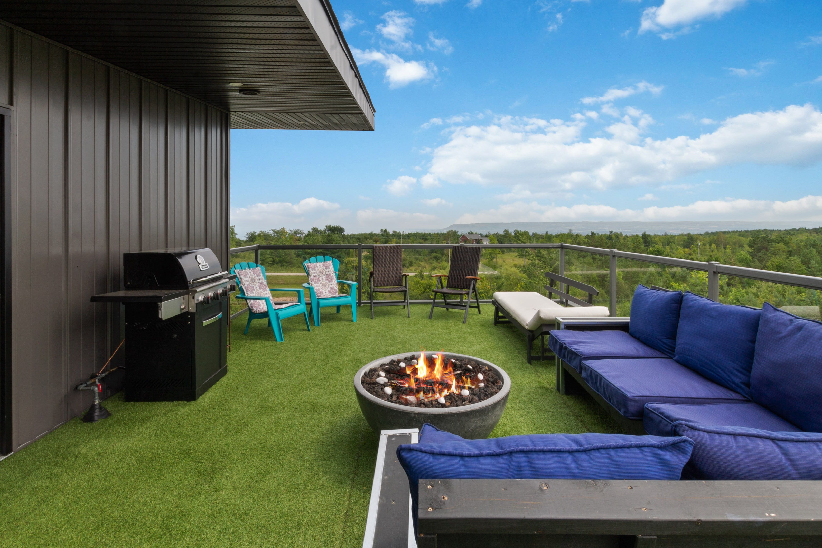 A barbecue, fire bowl and lounge seating arranged along the sheltered edge of the rooftop terrace