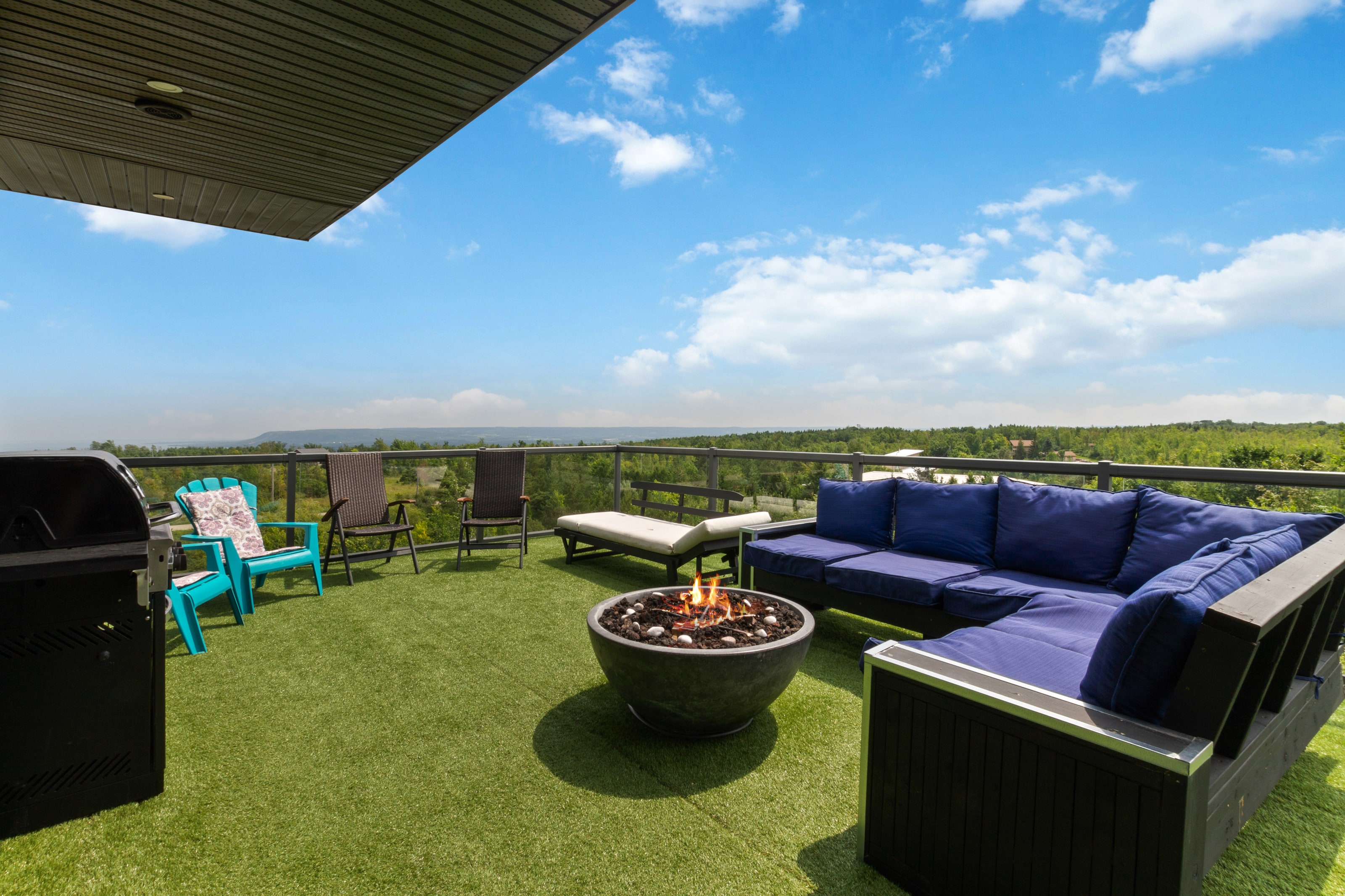 A lit gas fire bowl and navy sectional on the rooftop terrace, with the escarpment ridge and a strip of Georgian Bay on the horizon