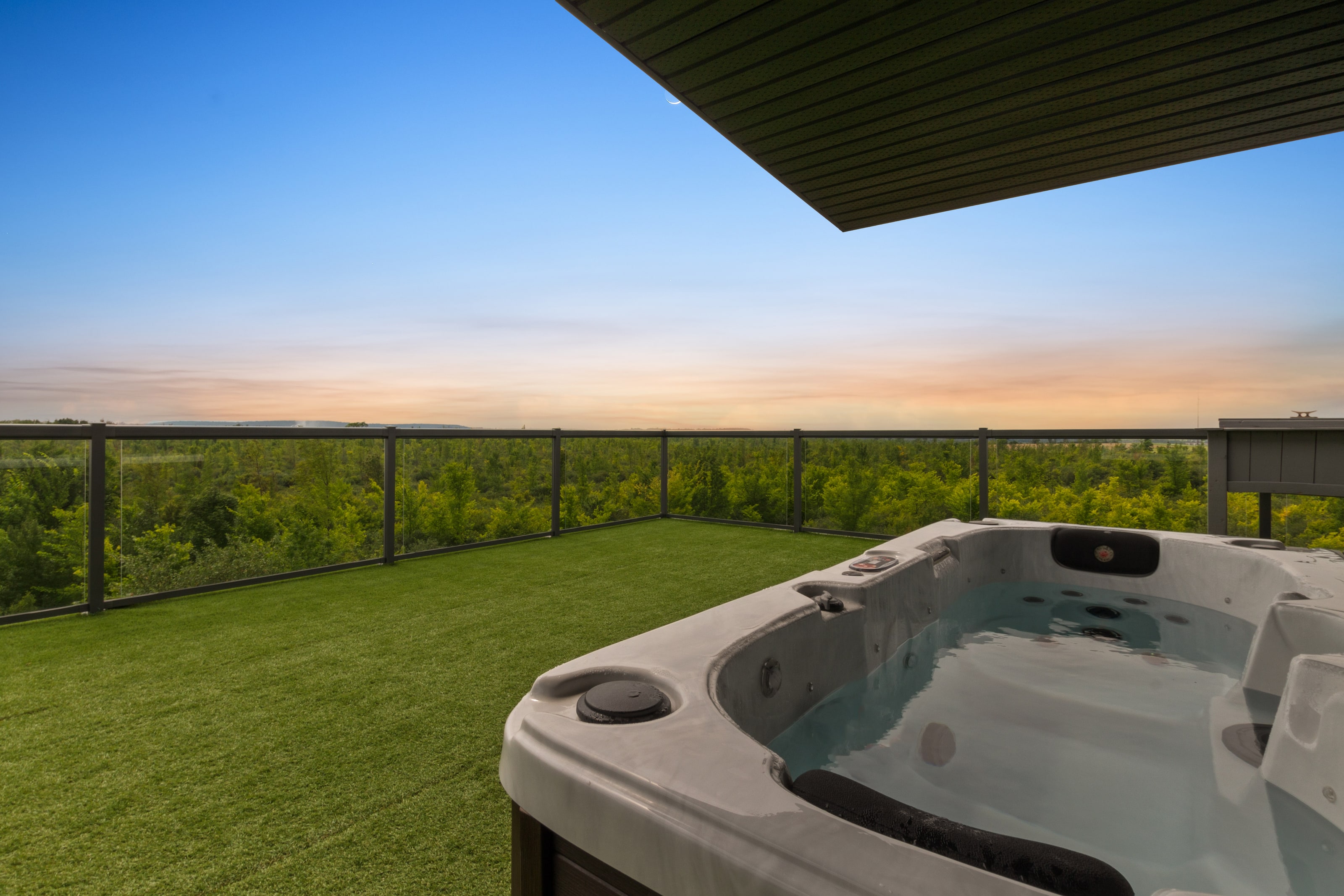 The rooftop hot tub with the sky turning gold over the tree line beyond the glass railing