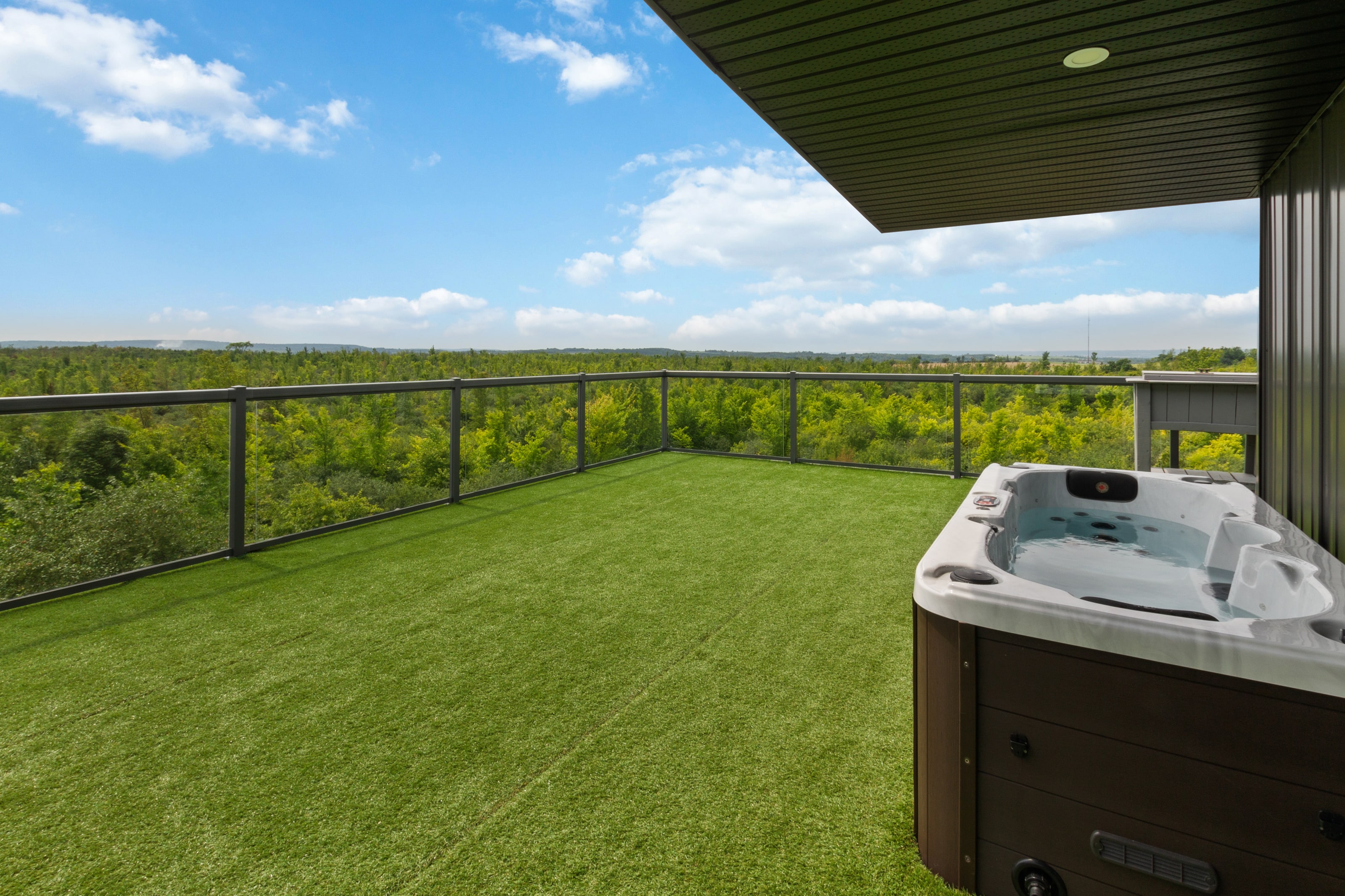 The open rooftop terrace laid with turf, hot tub to one side and glass railing all round