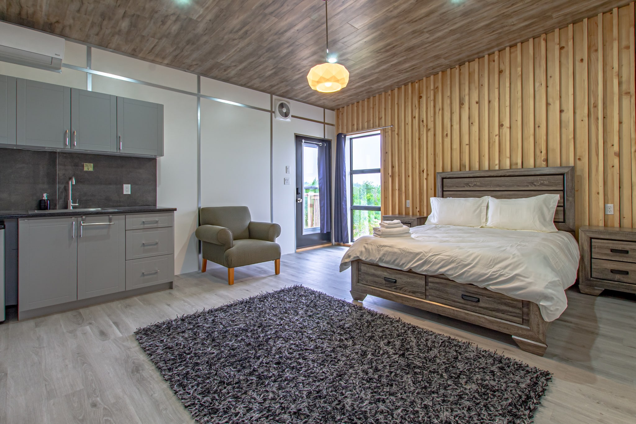 A guest suite with its own kitchenette, armchairs and a queen bed under a timber ceiling